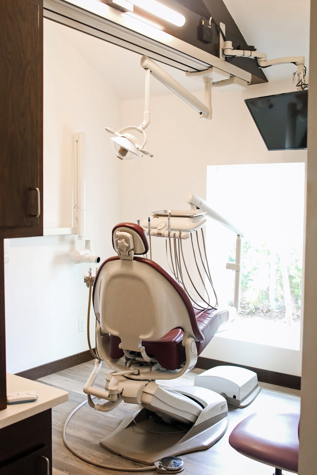 A dental office with a chair in the foreground and a ceiling-mounted dental equipment setup.