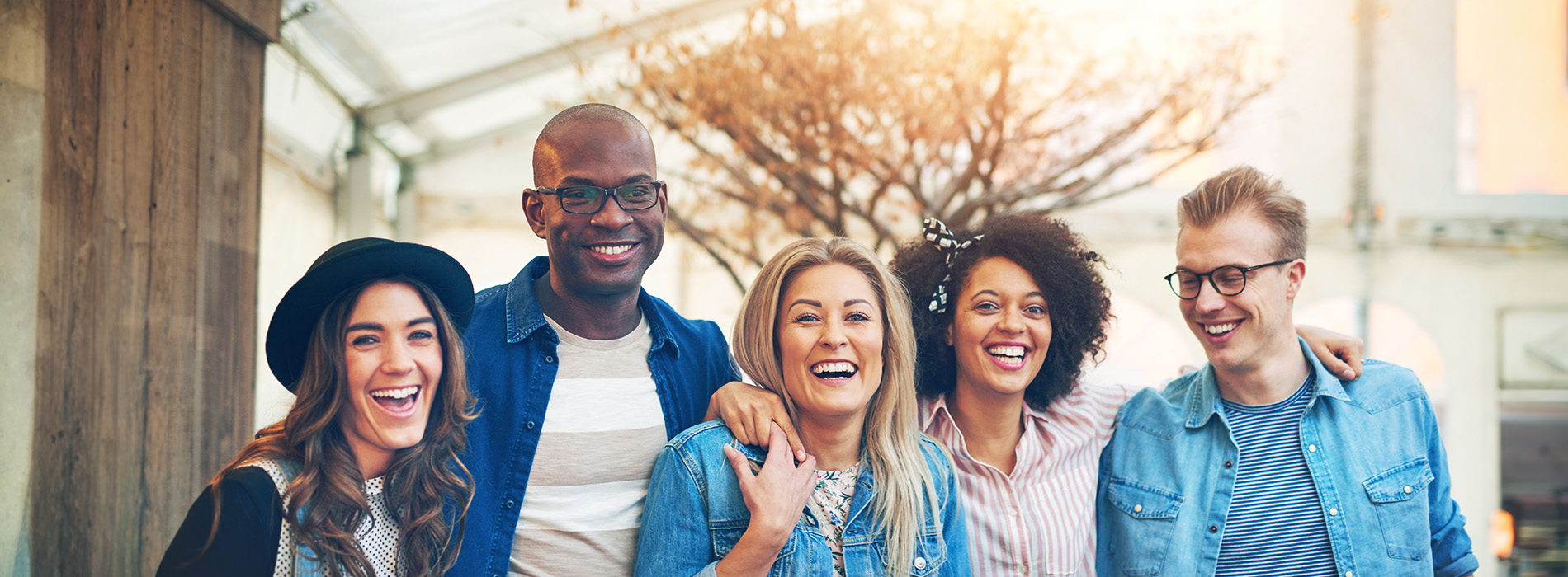 The image shows a group of five individuals posing together with smiles on their faces, standing outdoors during daylight hours.