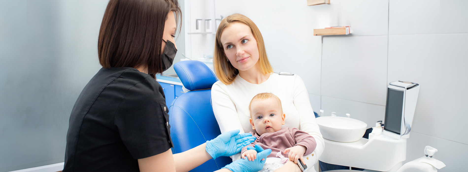 A woman and child are seated at a dental chair, receiving dental care from a dentist.