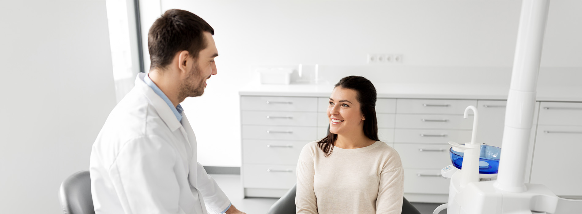 The image shows two people, likely professionals, engaged in conversation within an office setting, with a third person observing from behind.