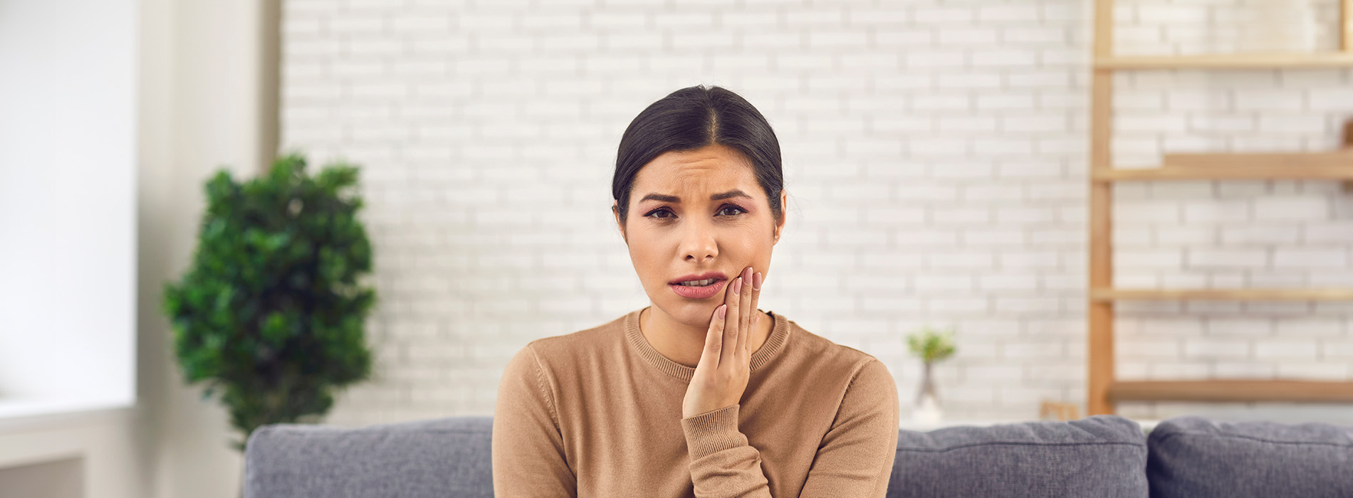 A woman sitting on a couch with her hand on her face, appearing surprised or concerned.