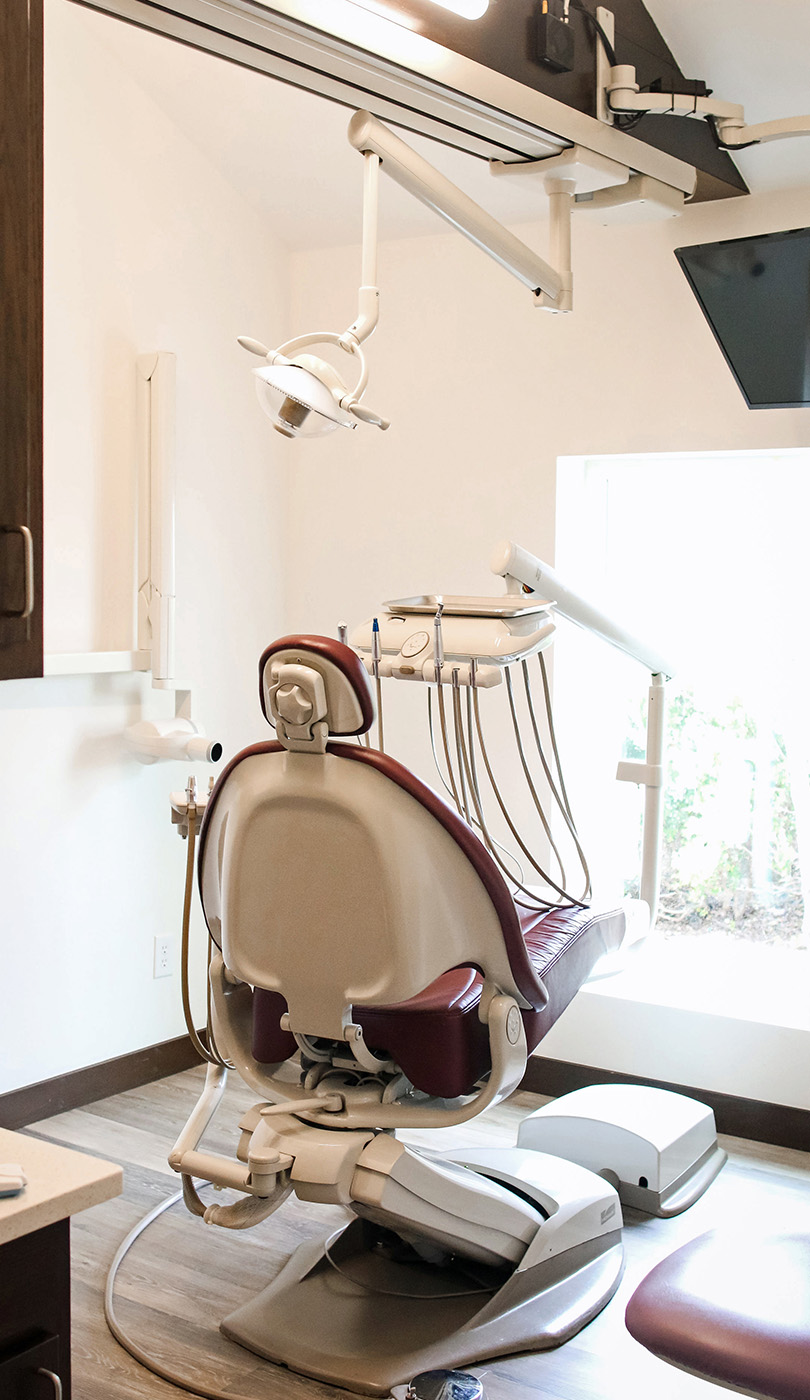 The image shows a dental office with a chair and various equipment, including a dental chair and overhead lights, set up for dental procedures.