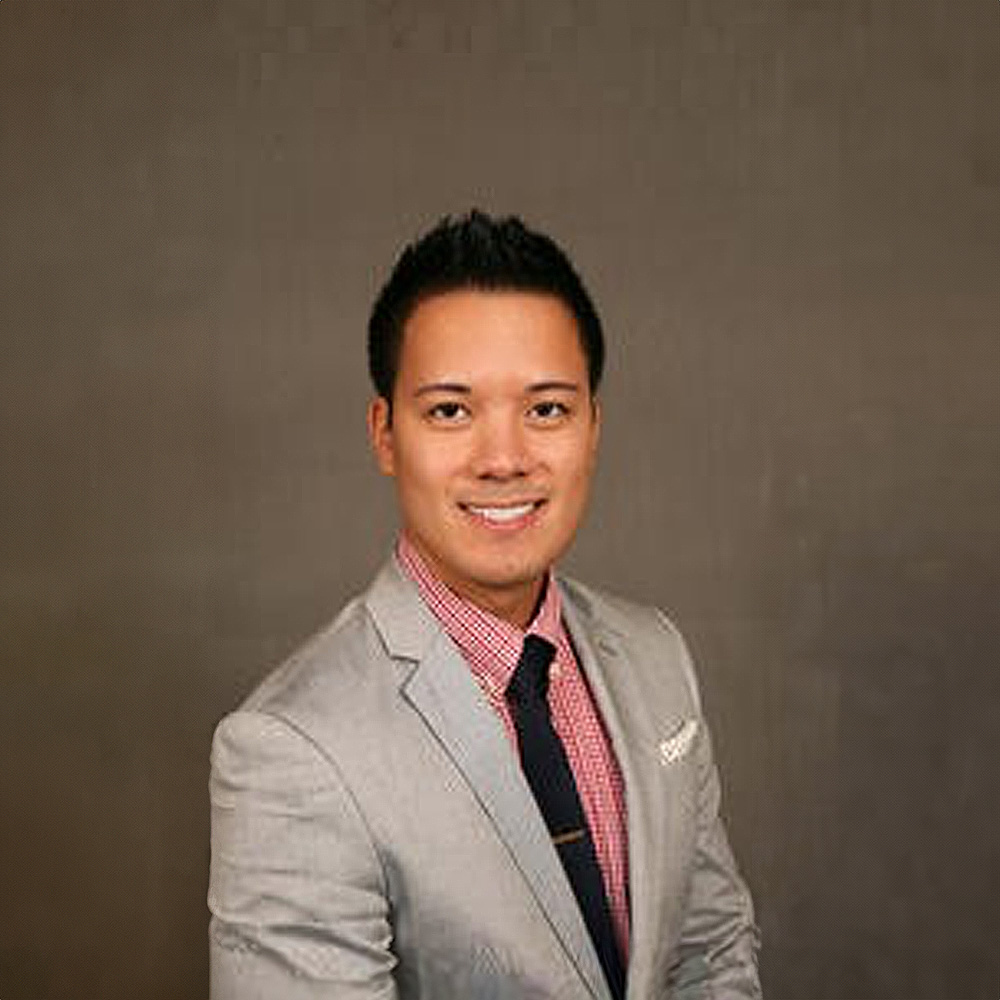 A smiling man wearing a suit and tie, standing against a neutral background.