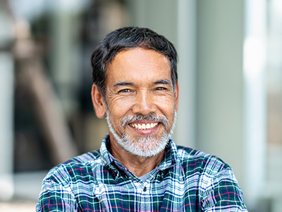 The image features a smiling man with a beard, wearing a plaid shirt, leaning against a wall.