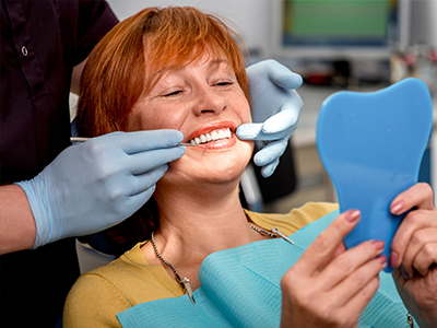 A woman sitting in a dental chair with a blue tooth mould on her face, being attended to by a dentist wearing gloves and a mask.