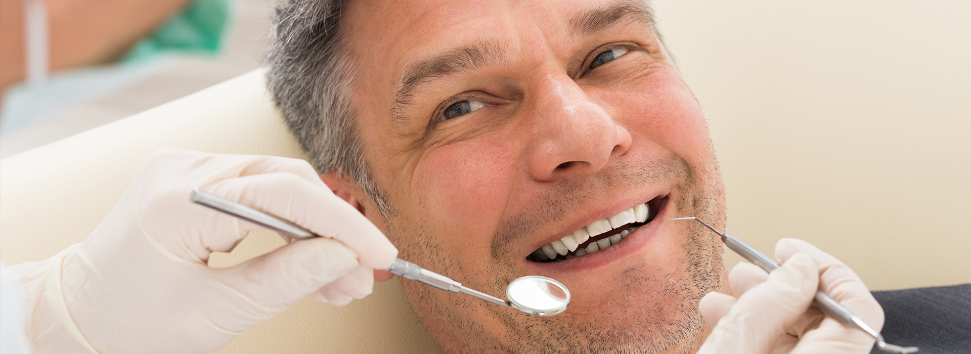 A man sitting in a dental chair with his mouth open, receiving dental care from a professional using a drill.