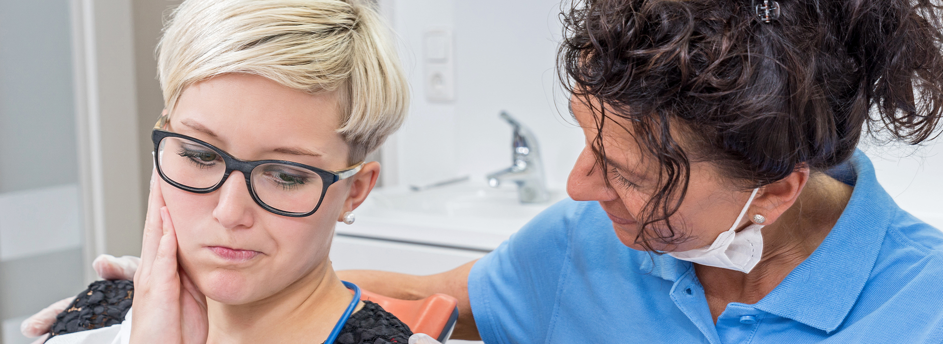 Woman with glasses looking at another woman s face while sitting in a dental chair.