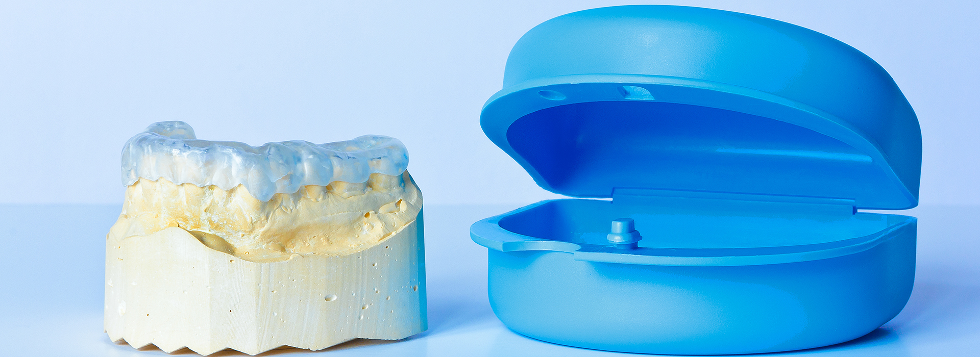 The image shows a blue dental crown next to a yellow toothbrush head.