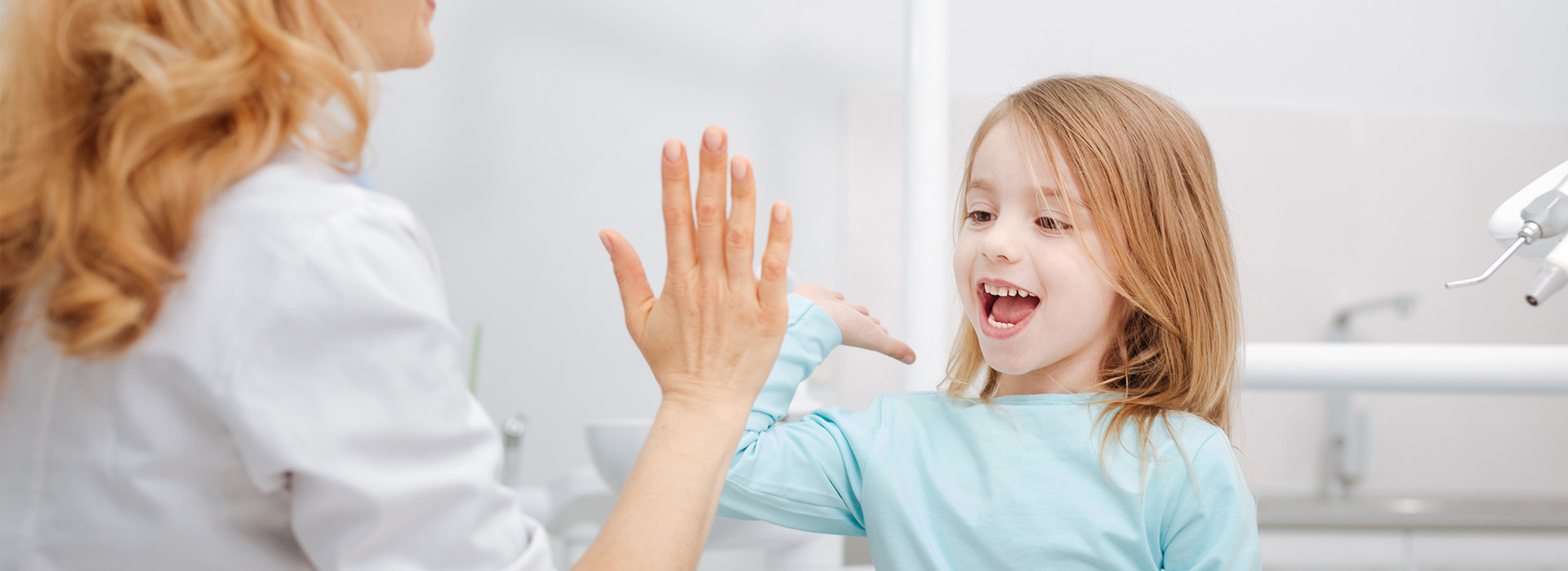 A young girl with brown hair is waving at a woman who is smiling and appears to be interacting with her, while another person looks on.