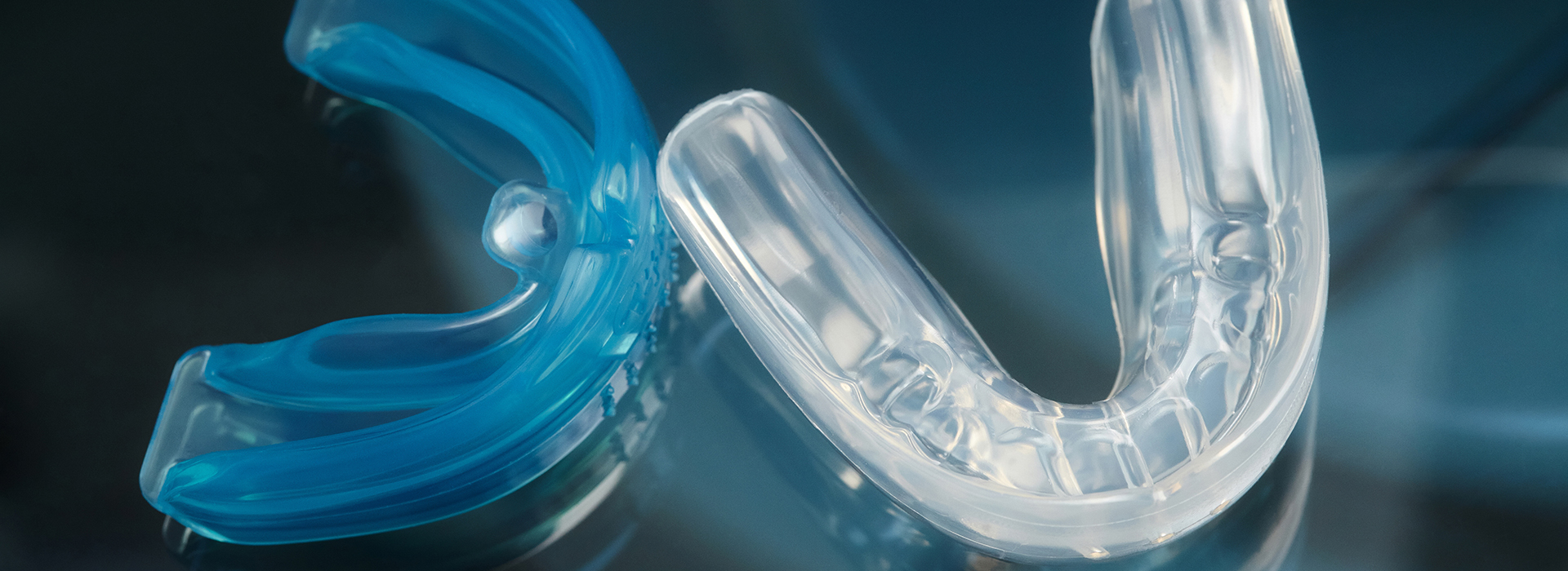 The image displays a close-up view of clear plastic dental retainers with blue accents against a blurred background.