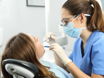 A dental hygienist working on a patient s teeth with professional tools while wearing protective gear.