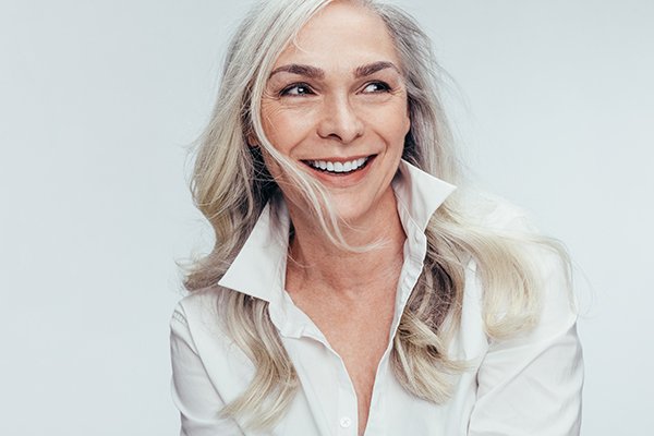 The image shows a woman with short hair smiling at the camera while wearing a white blouse.
