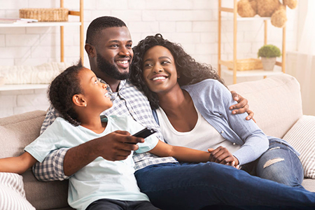 A family of four sitting on a couch with a warm, happy expression, smiling at the camera.