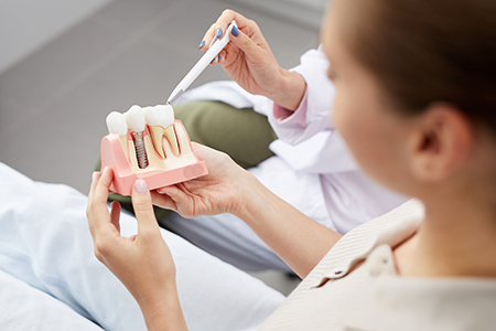 A woman holding up a dental model with an instrument while sitting in a dental office.