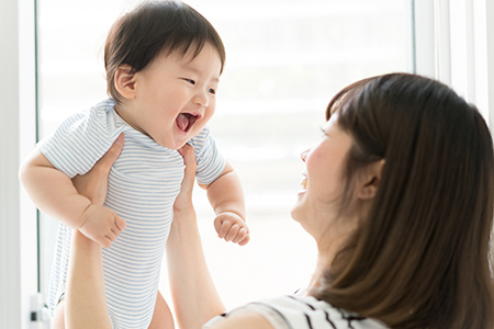A woman holding a baby while smiling at the camera.