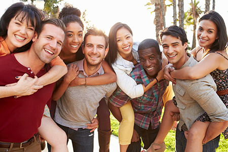The image shows a group of young adults posing together outdoors, smiling and embracing each other.