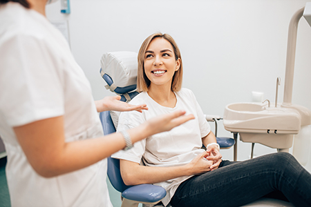 A woman seated in a dental chair with a smile, being attended to by two dental professionals who are engaged in conversation.