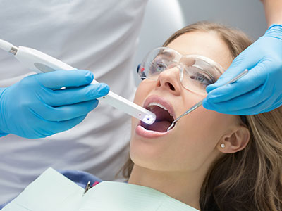 A woman receiving dental treatment with a device, surrounded by medical professionals wearing blue gloves and face masks.