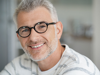 The image shows a man with glasses smiling at the camera, looking directly ahead.