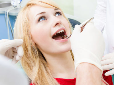 A woman seated in a dental chair receiving dental treatment, with a dentist performing the procedure while wearing protective gloves and a face mask.