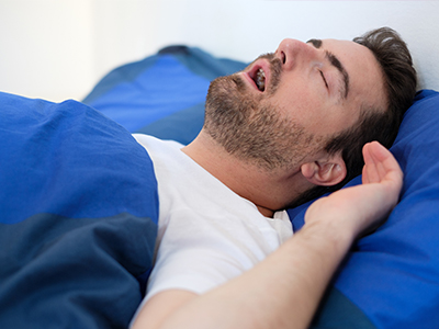 A man sleeping on a bed with blue sheets and pillows.