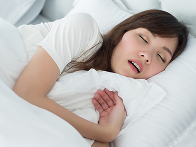 A young woman asleep with her eyes closed, lying on a bed with white sheets and pillows.